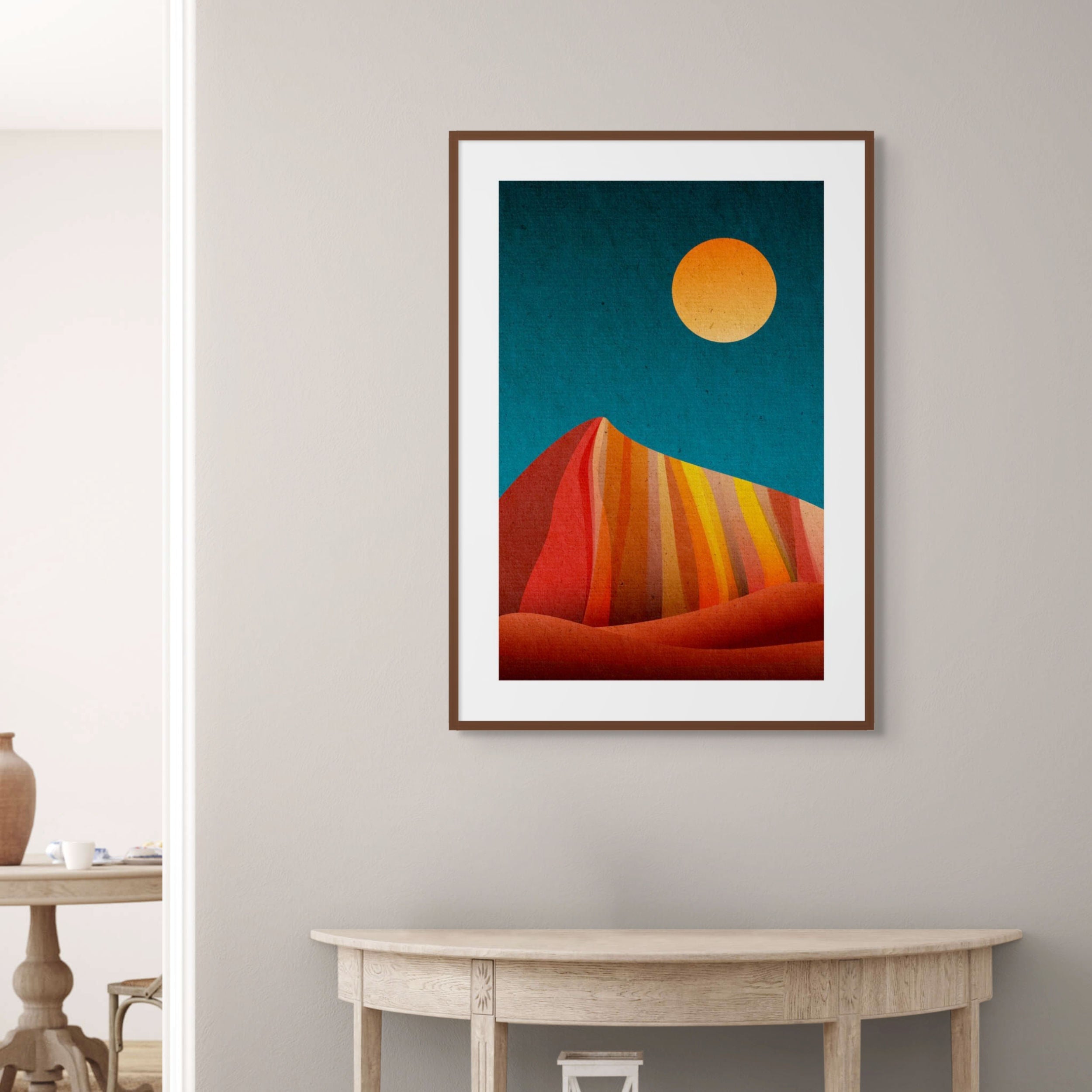 Geometric abstract print with layered warm-toned mountain forms beneath a golden sun.