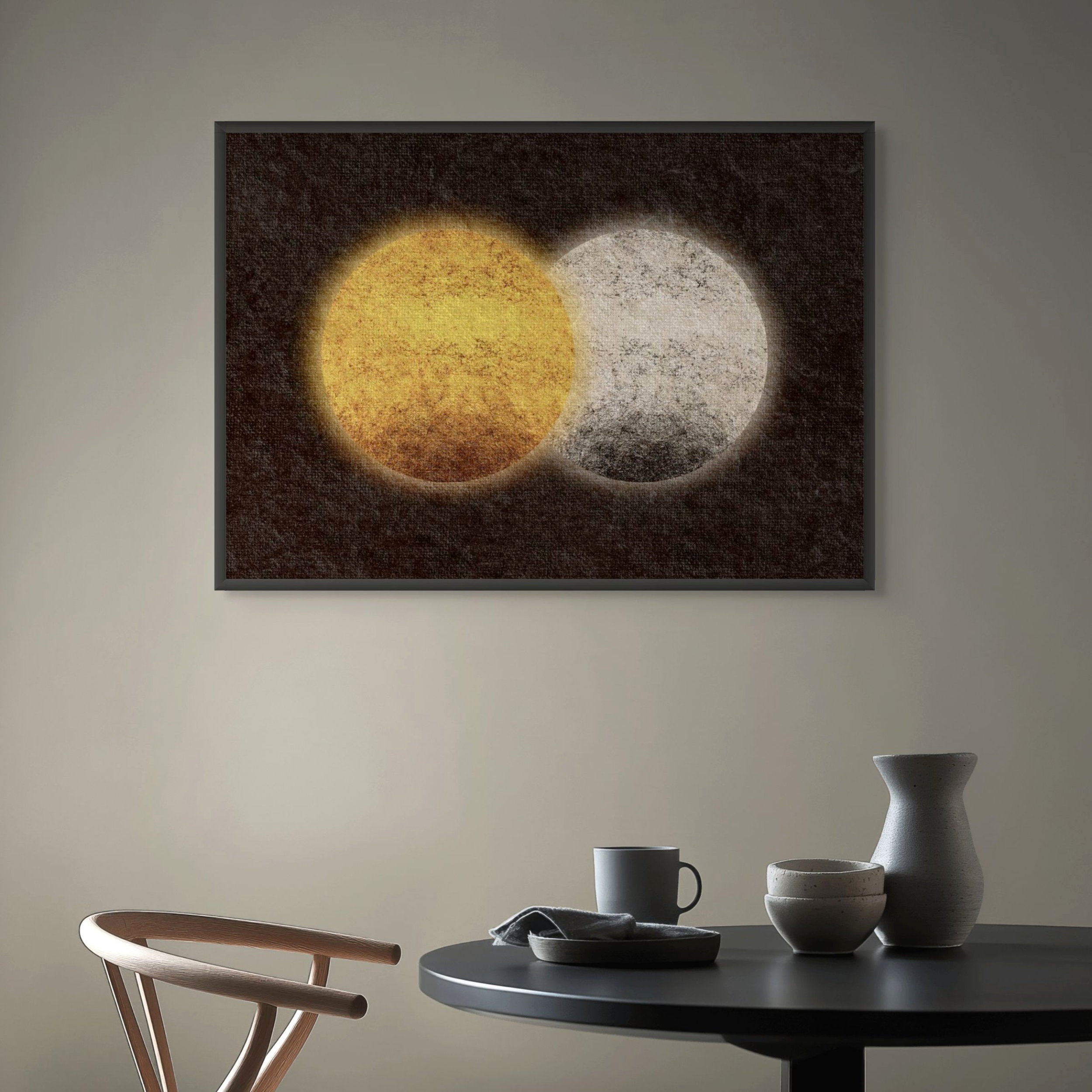 Abstract sun and moon art print featuring overlapping golden and pale circular forms on a dark textured background, displayed in a frame above a minimalist dining table.