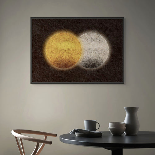 Abstract sun and moon art print featuring overlapping golden and pale circular forms on a dark textured background, displayed in a frame above a minimalist dining table.