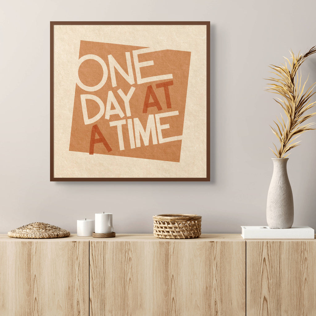 One Day at a Time typographic wall art styled above a wooden sideboard in a calm modern living room with neutral decor